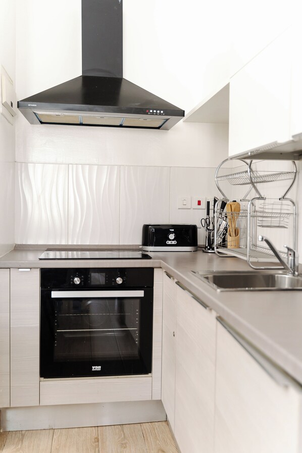 A modern kitchen with a built-in oven, a stainless steel range hood, and a sink with a drying rack.