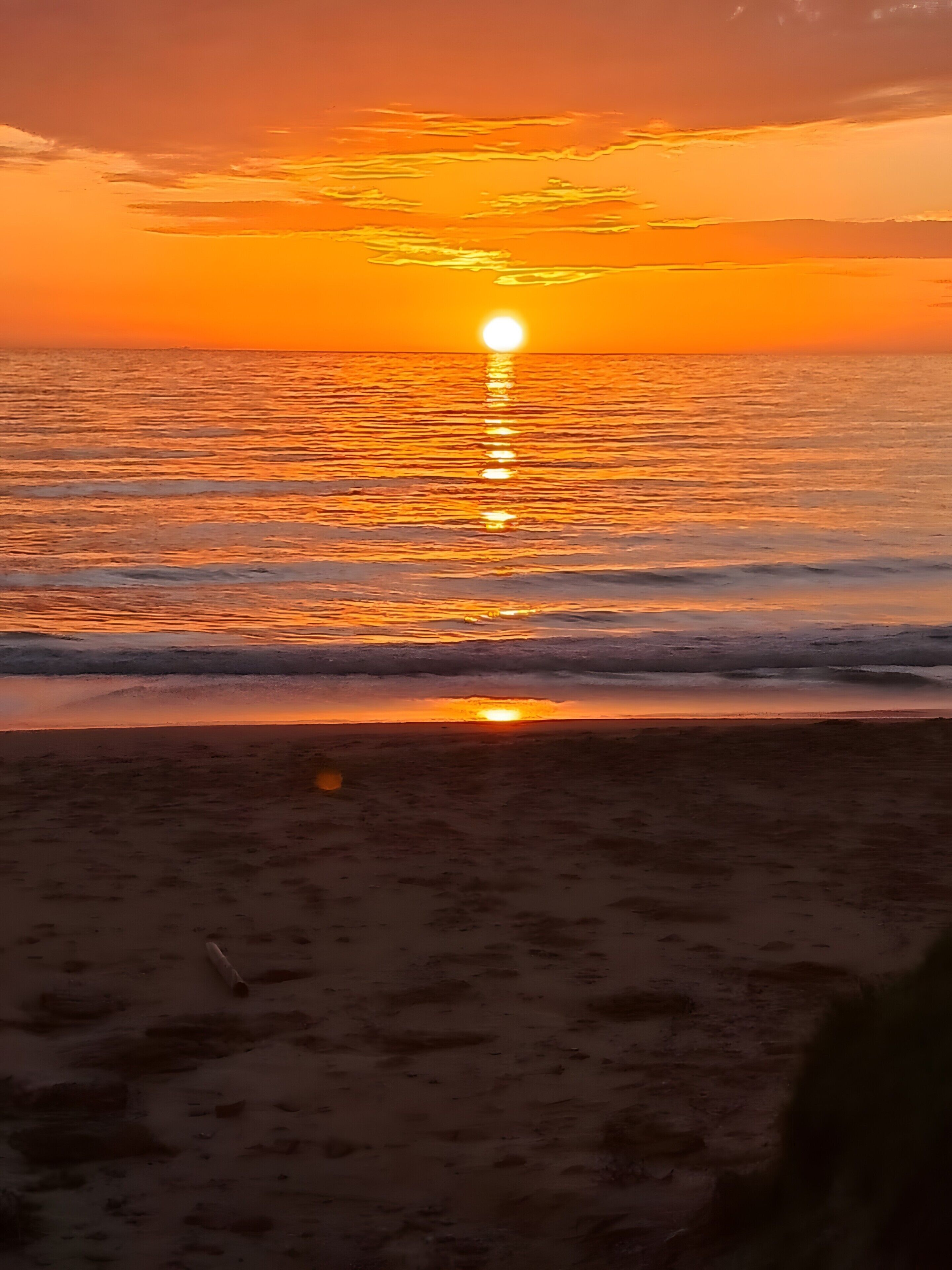 A sunset over a beach with waves gently lapping at the shore.