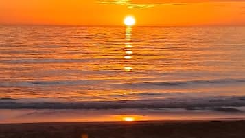 A sunset over a beach with waves gently lapping at the shore.