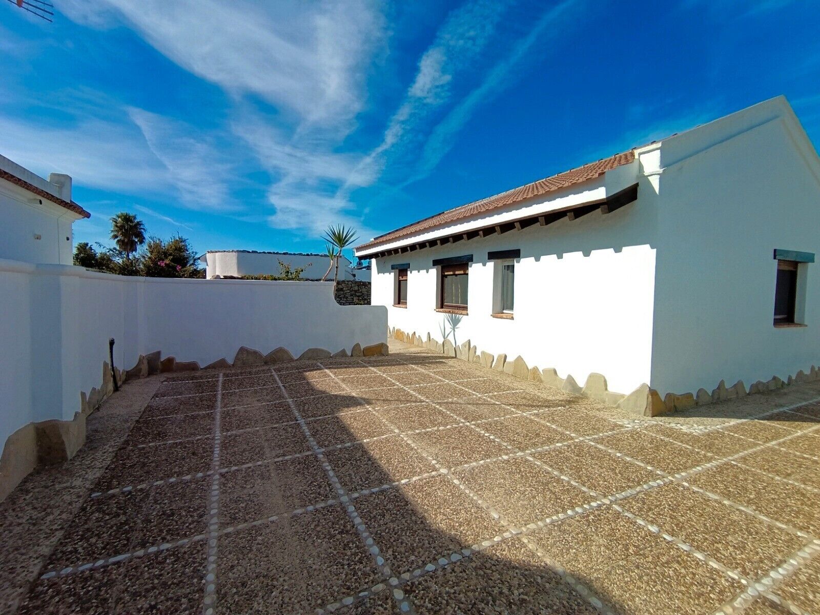A white building with a tiled patio and a clear blue sky.