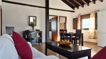 A living room with a sofa, a dining table with chairs, a TV, and a kitchen area with a window.