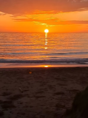 A sunset over a beach with waves and a clear sky.