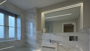 Une salle de bain moderne dotée d’une douche à paroi de verre, d’un meuble-lavabo recouvert de carreaux de marbre et d’un grand miroir.
