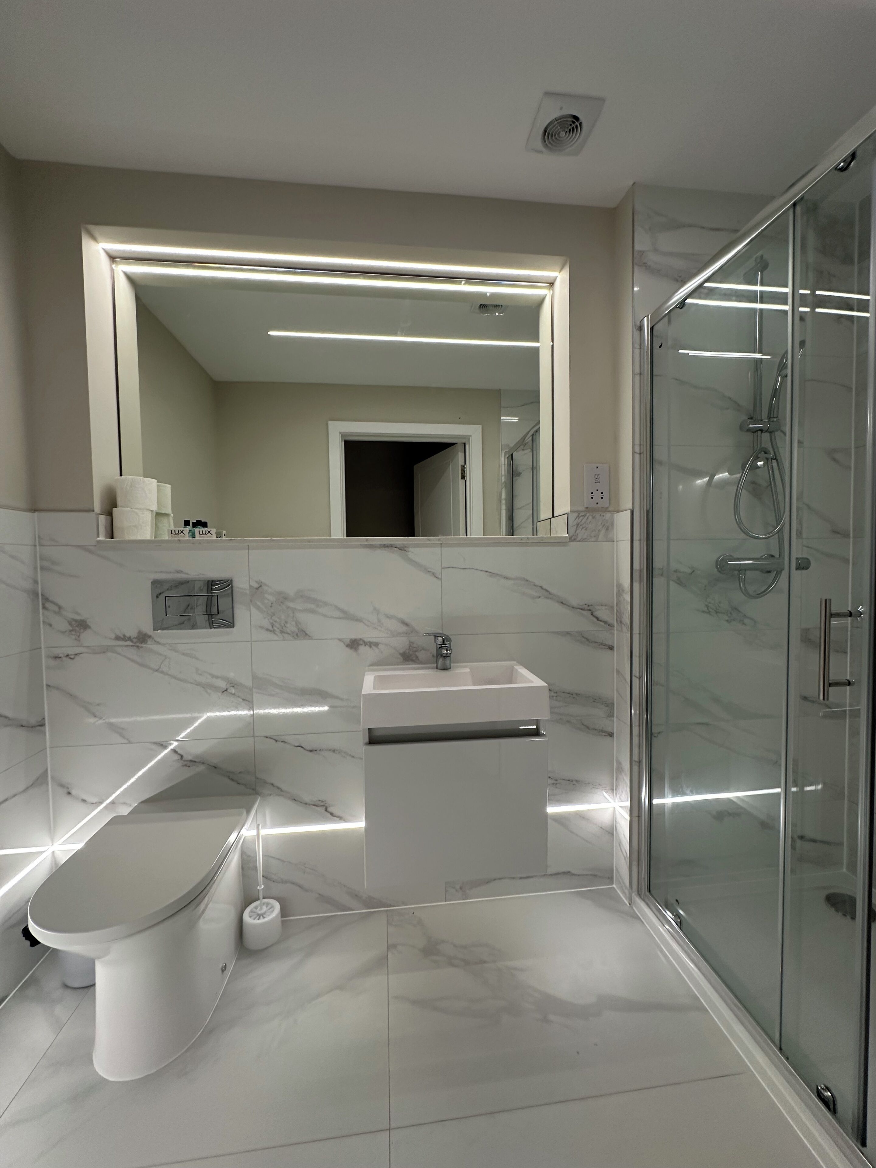 A modern bathroom with a glass shower enclosure, a white sink, and a large mirror.