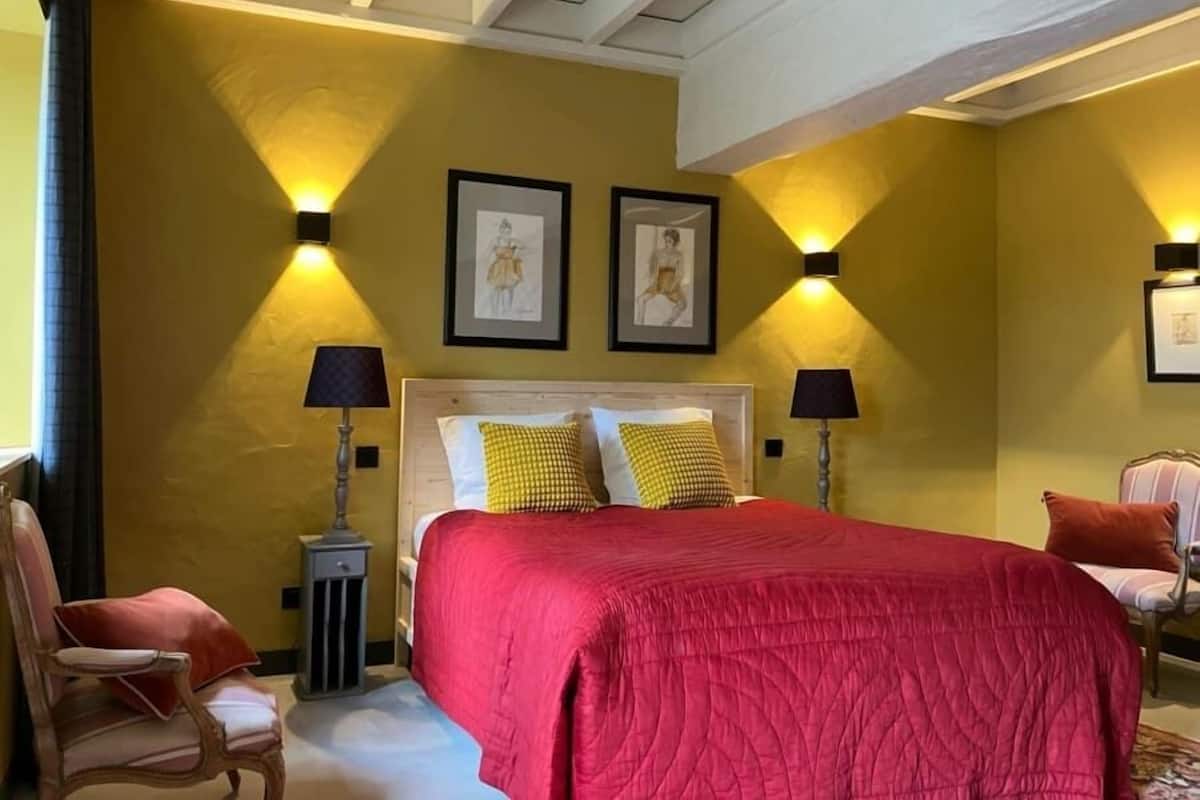 A room with a bed, two wall-mounted lamps, and two framed pictures.