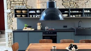 Una cucina moderna con parete in pietra, una grande lampada a sospensione nera e un tavolo da pranzo in legno con sedie.