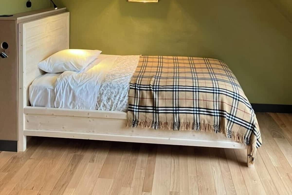 A bedroom with a sloped ceiling, a bed with a plaid blanket, a nightstand, and a wall-mounted picture.