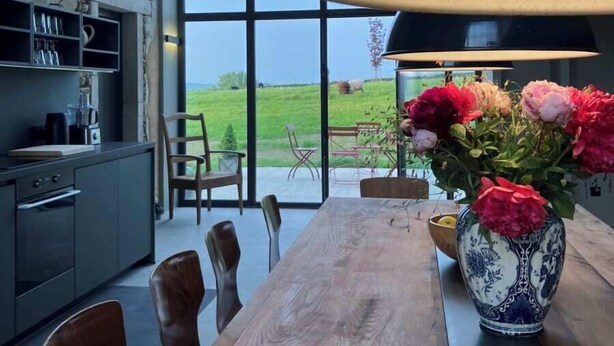 Una cucina moderna con un'ampia finestra, un tavolo da pranzo in legno con sedie e un vaso di fiori.