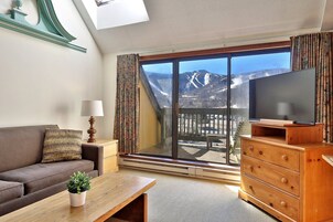 Una sala de estar moderna con un gran ventanal corredera que da a un balcón con vistas a la montaña.