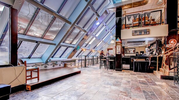 A restaurant with a high ceiling and skylights, featuring a bar area with stools and a seating area with tables and chairs. - Mountain Green Resort (Killington)