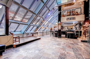 Un restaurante con techo alto y tragaluces, que cuenta con una zona de bar con taburetes y un área de comedor con mesas y sillas.
