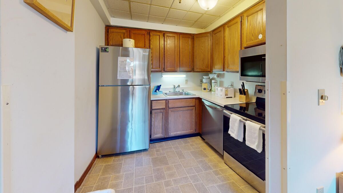 Una cocina compacta con armarios de madera, un refrigerador de acero inoxidable, un microondas y un horno.