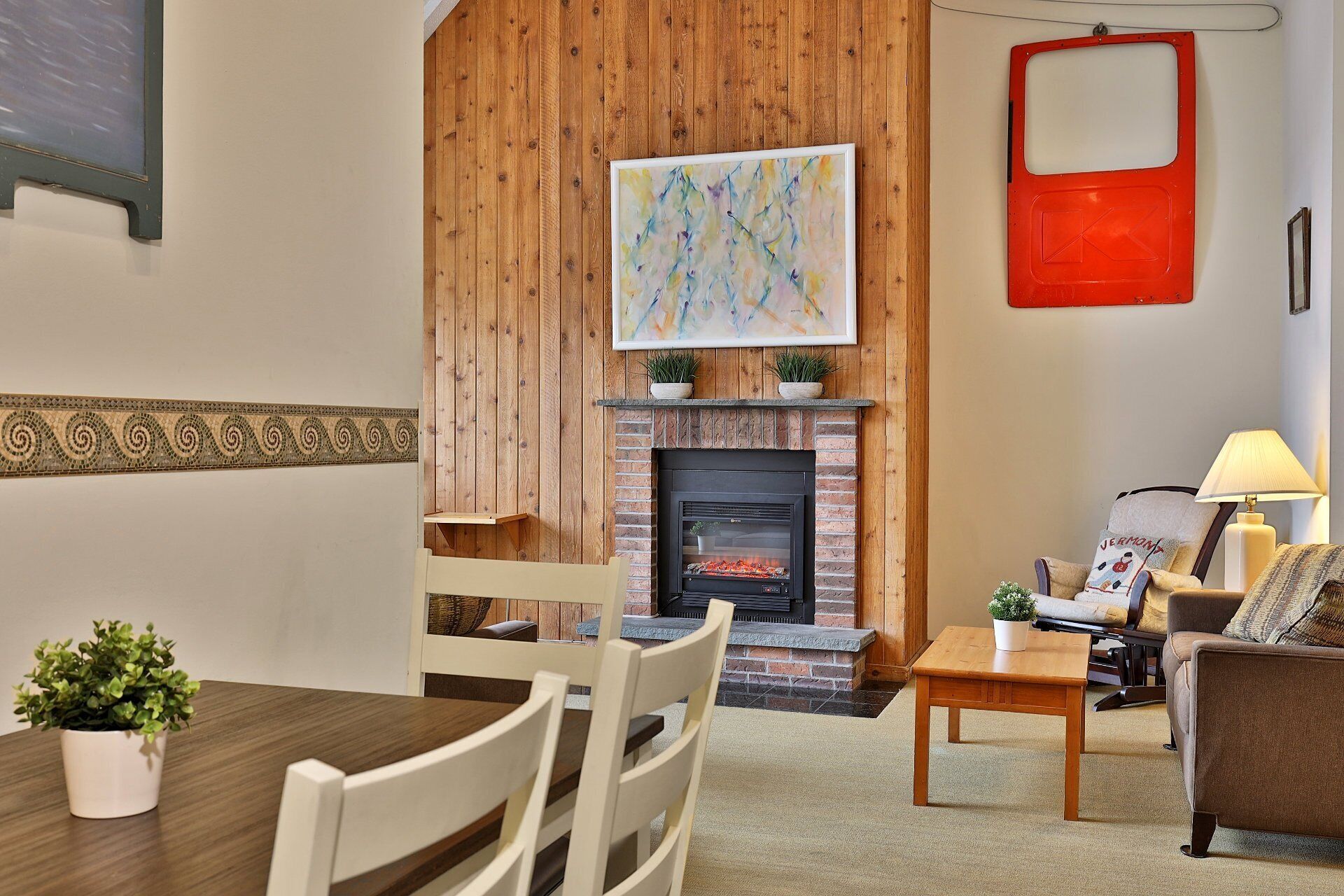 A cozy living room with a fireplace, wooden paneling, a dining table with chairs, and a sofa.