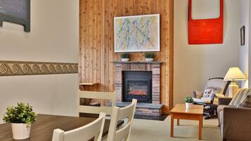 A cozy living room with a fireplace, wooden paneling, a dining table with chairs, and a sofa.