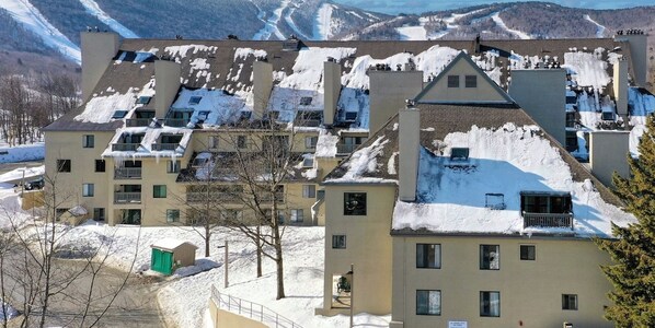 Un edificio de varios pisos con tejados cubiertos de nieve y una vista de una pista de esquí al fondo.