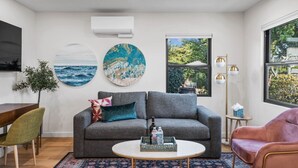 Una sala moderna con un sofá gris, una mesa redonda de centro y un ventanal con vistas a zonas verdes.