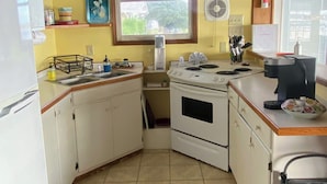 A compact kitchen with white cabinets, a stove, and a sink. There is a window providing natural light and a view of greenery outside. - Water Lovers Retreat: stunning water views - dolphins for neighbors (Peletier)
