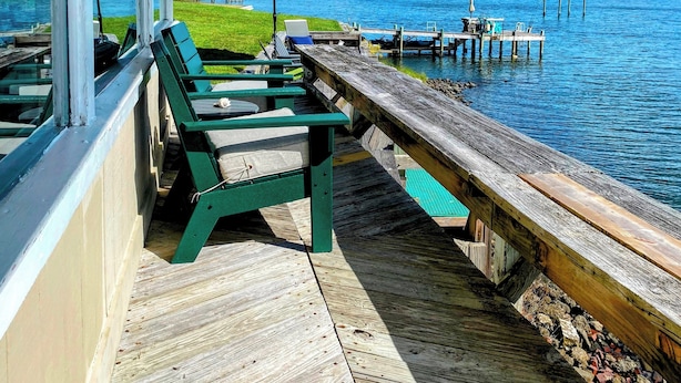 A covered deck with green chairs and a table overlooking a lake, with a dock extending into the water. - Water Lovers Retreat: stunning water views - dolphins for neighbors (Peletier)