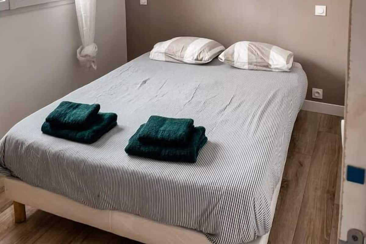 A bedroom with a bed, two pillows, a window with curtains, and a wall-mounted light fixture.