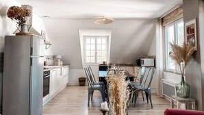 A modern kitchen with a dining area, featuring a wooden ceiling, white cabinetry, and a large window. - La Maison Alfred (Arzal)