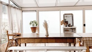 A dining area with a wooden table, bench, and chairs. There is a potted plant and a vase with dried flowers on the table. - La Maison Alfred (Arzal)