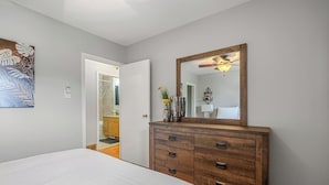 Een slaapkamer met een bed, een houten dressoir, een spiegel en een deur naar een badkamer.