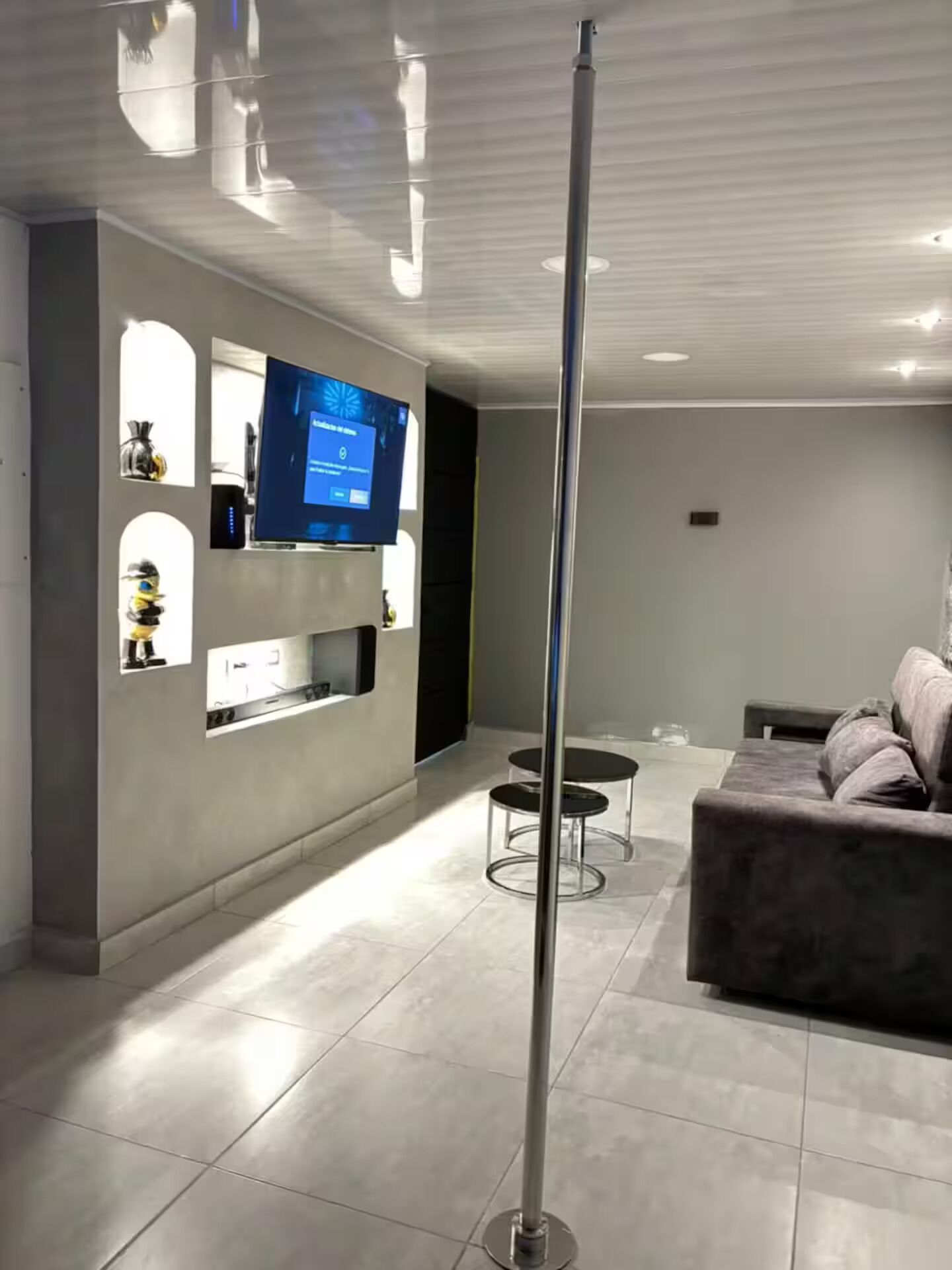 Ein modernes Wohnzimmer mit einem an der Wand befestigten Flachbildfernseher, einer Couch, einem Couchtisch und einer stehenden Stehlampe.