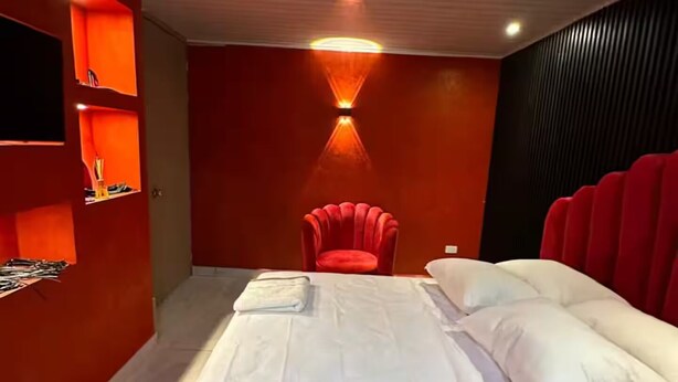 Un dormitorio moderno con cama, sillón rojo y estanterías empotradas.