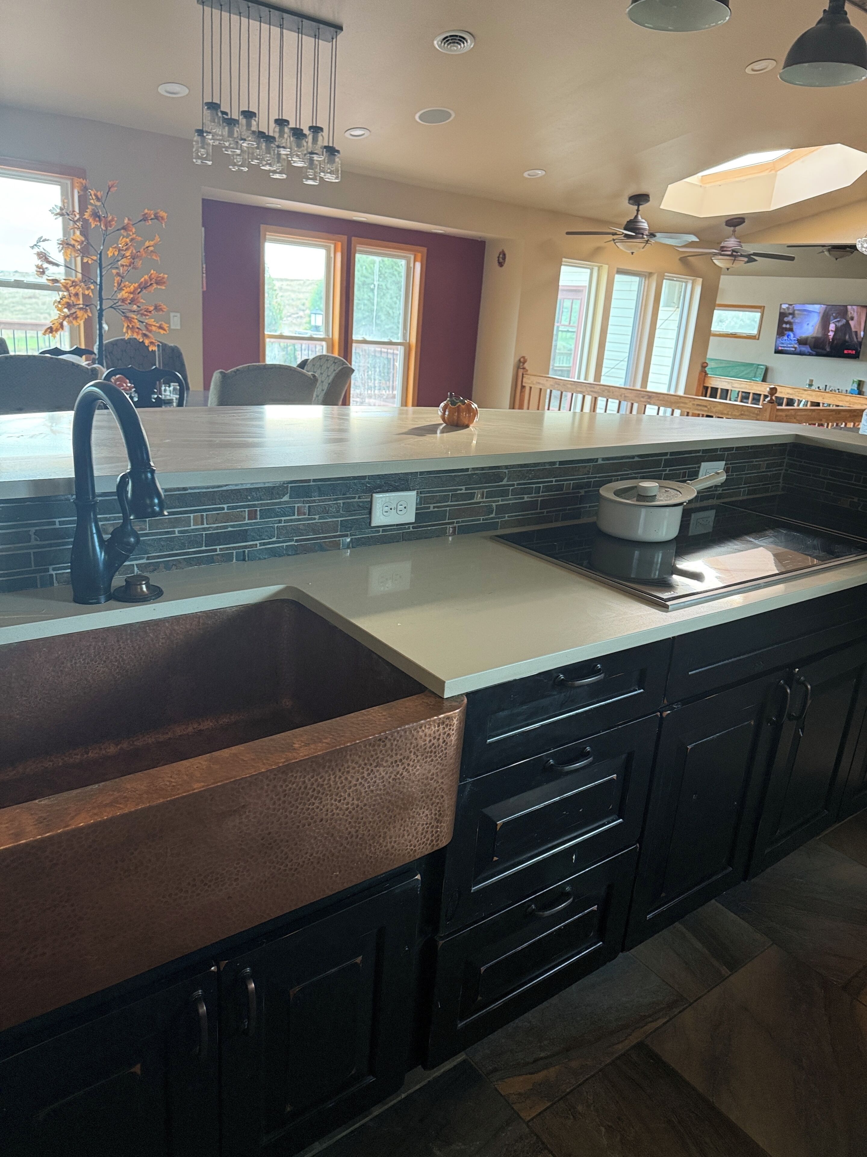 A kitchen with a large island, black cabinets, a stainless steel sink, and a ceiling fan.