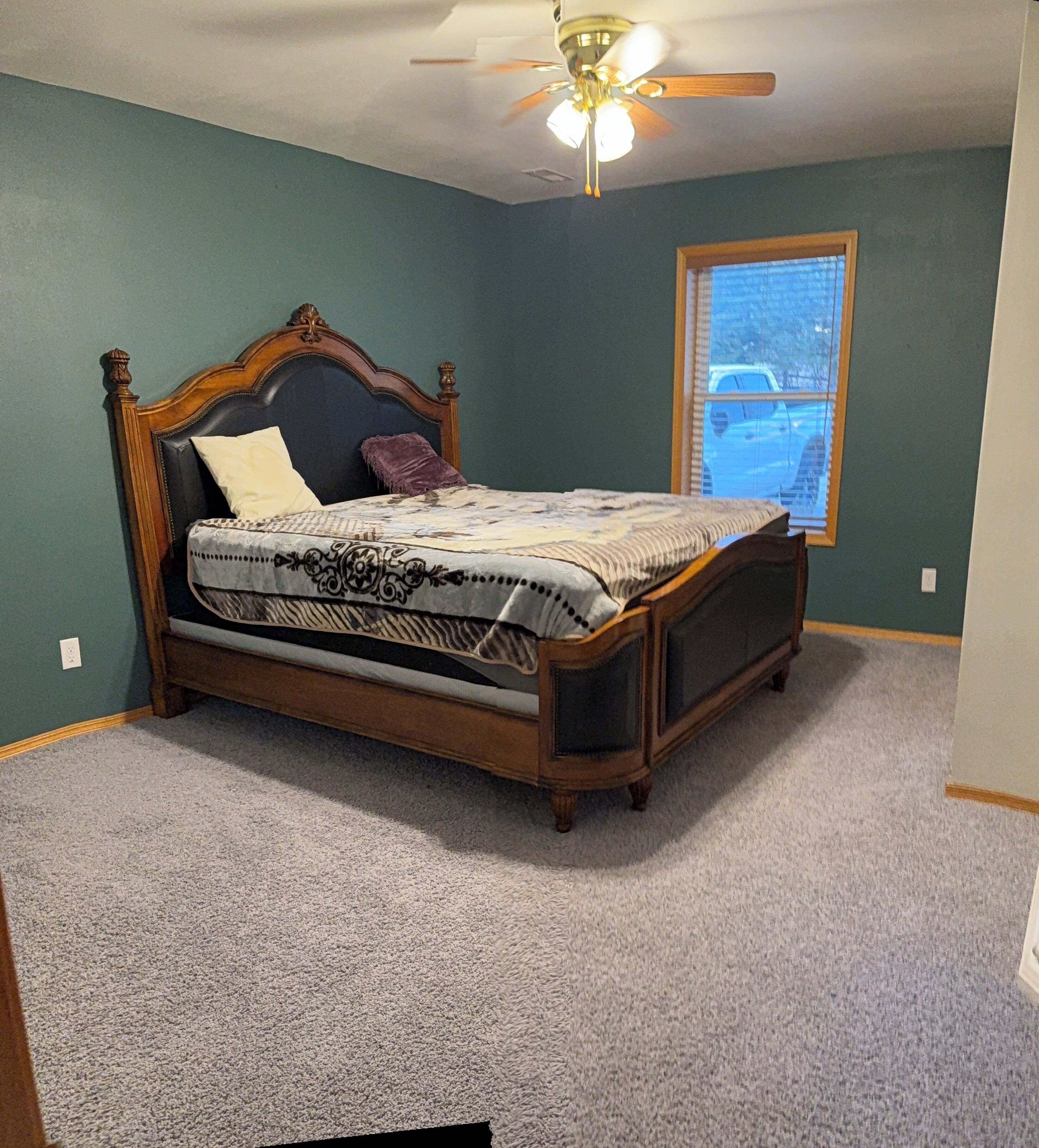 A bedroom with a bed, a ceiling fan, a window with a view of a parking lot, and green walls.