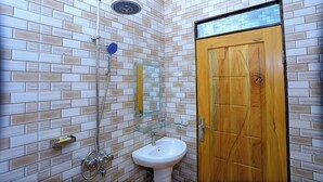 A bathroom with a tiled wall, a wooden door, a glass shower enclosure, and a pedestal sink.
