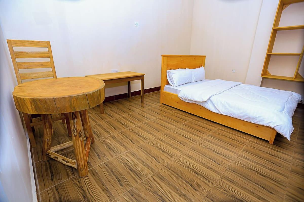 A room with a wooden bed, a wooden chair, and a small round table.