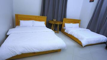 Two single beds with wooden headboards in a room with white walls and grey curtains.