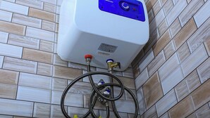 A white water heater with a blue control panel, mounted on a tiled wall.