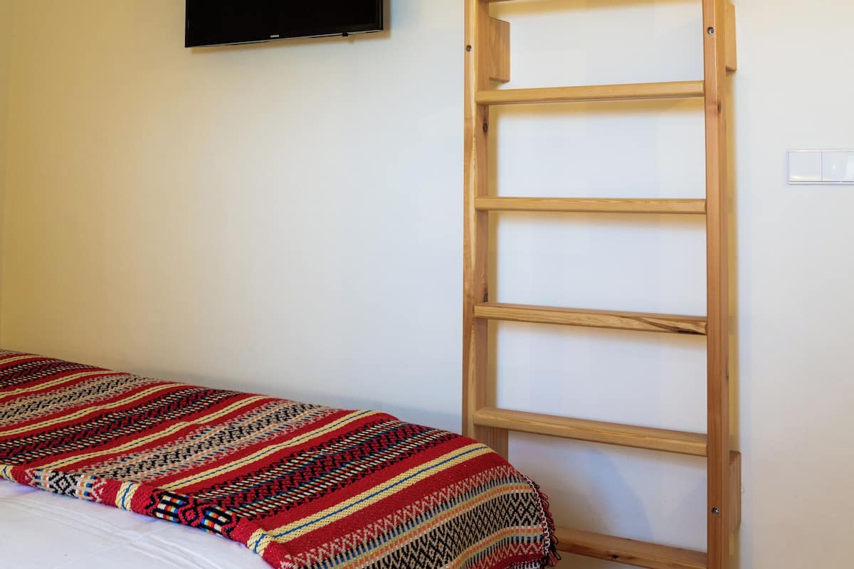 Un dormitori amb un llit, una escala de fusta, una televisió penjada a la paret i una manta amb dibuixos.