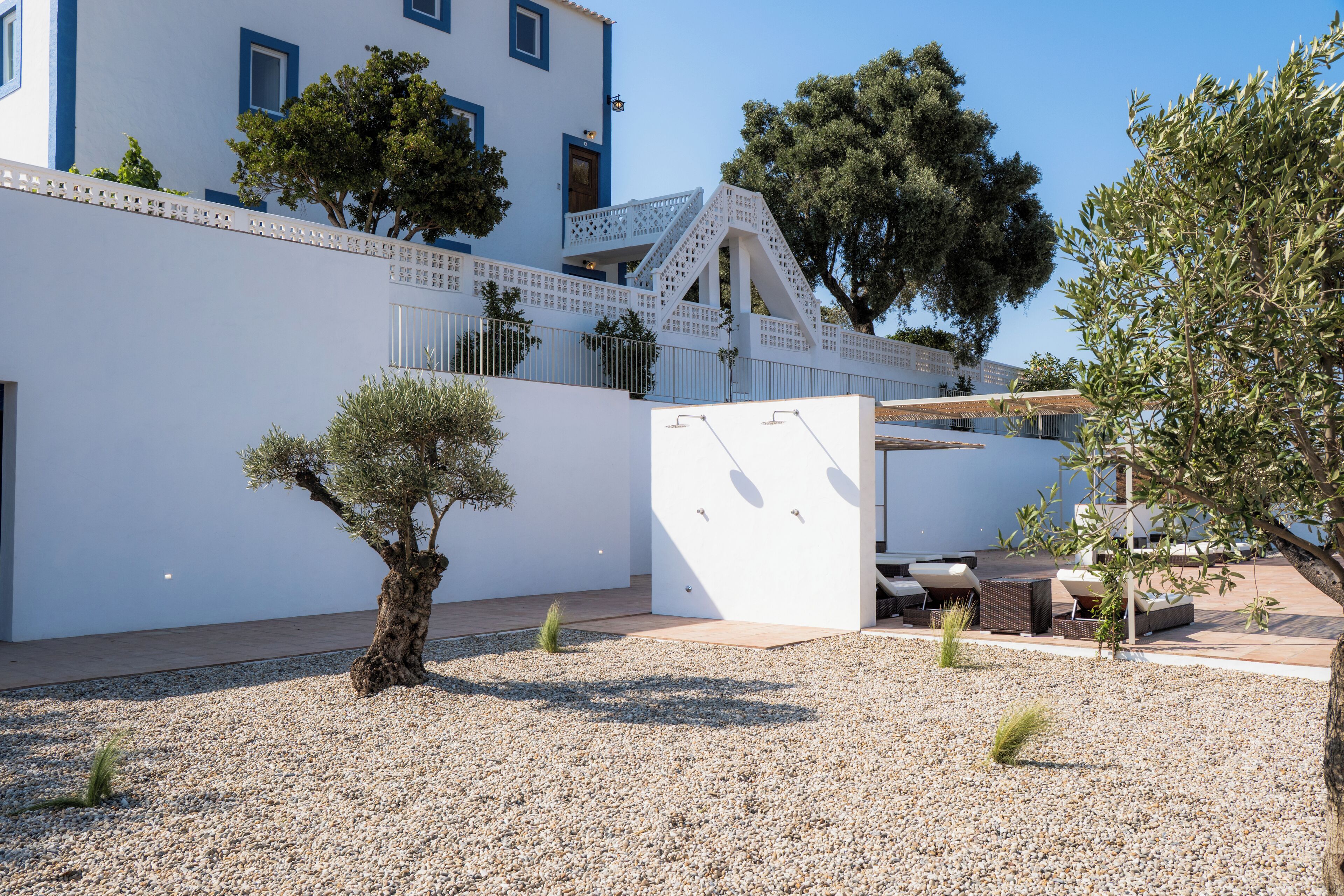 Ein modernes Gebäude mit weißer Fassade, einem kleinen Garten mit Kies und Sitzgelegenheiten im Freien.