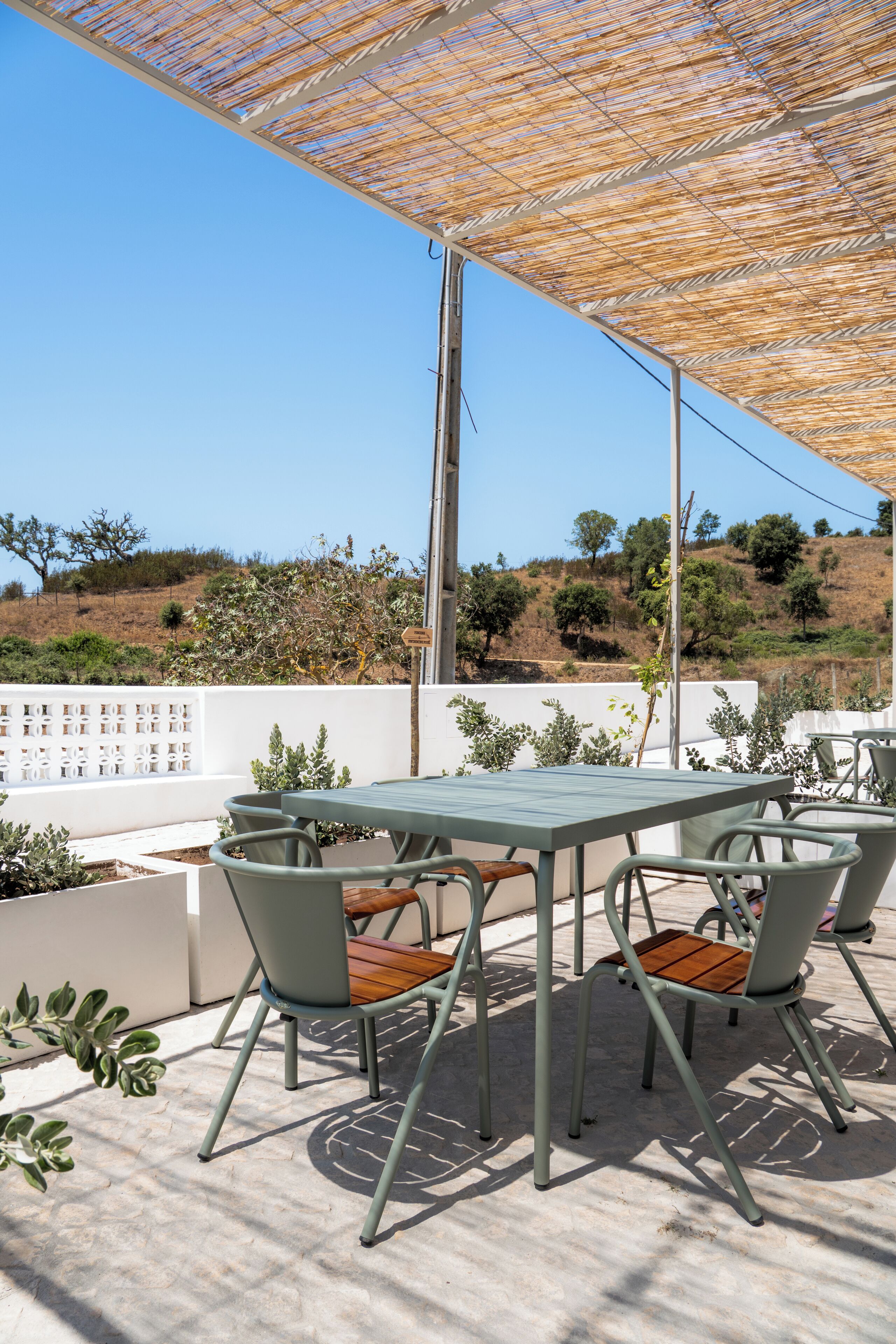 An outdoor patio with a table and chairs, a pergola providing shade, and a view of a hilly landscape.