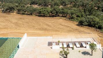 An aerial view of a property with a swimming pool, a patio area, and a view of a forested landscape.