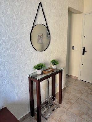A hallway with a glass-top console table, two potted plants, a mirror, and a door with a lock. - Apartment 57, Air Conditioning, Sea View, WiFi, Parking Space, Complete. (Praia Grande)