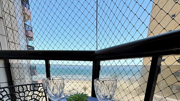 A table set with blue placemats and clear glassware on a balcony overlooking a beach. - Apartment 57, Air Conditioning, Sea View, WiFi, Parking Space, Complete. (Praia Grande)