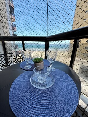 A table set with blue placemats and clear glassware on a balcony overlooking a beach. - Apartment 57, Air Conditioning, Sea View, WiFi, Parking Space, Complete. (Praia Grande)