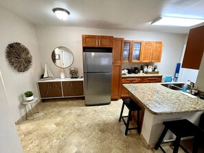 A kitchen with a central island, wooden cabinets, a stainless steel refrigerator, and a tiled floor.