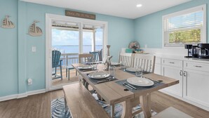 A dining area with a view of the sea, a kitchen with white cabinets, and a sign above the door that reads "Take Me To The Sea". - Sandy Sunset Sound front 4BR Home Two Decks w/ Sunset Views Boat Dock (Navarre)