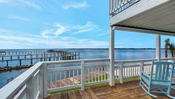A wooden deck with a white railing overlooking a calm body of water and a dock. - Sandy Sunset Sound front 4BR Home Two Decks w/ Sunset Views Boat Dock (Navarre)