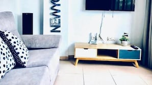 Ett modernt vardagsrum med en grå soffa, ett TV-bord i trä och en väggmonterad platt-TV.