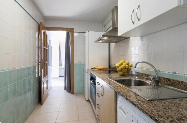 A narrow kitchen with a granite countertop, stainless steel sink, and a built-in oven.