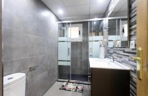 Ein modernes Badezimmer mit Duschkabine aus Glas, einem weißen Waschbecken und einem Spiegel mit Holztür.
