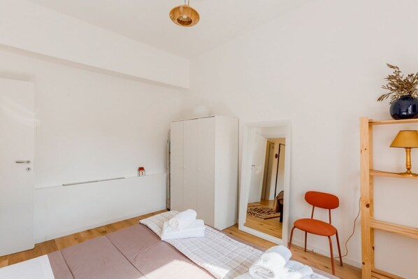 A bedroom with a bed, a wardrobe, a mirror, a chair, and a shelf with a lamp.