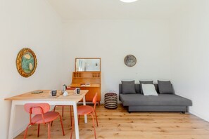 A room with a wooden table, two red chairs, a grey sofa, a wooden bookshelf, and a round side table.