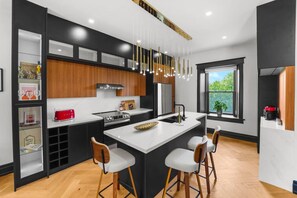 A modern kitchen with a central island, bar stools, and a large window offering a view of greenery. - Historical Loft Retreat Minutes to Elora Main St (Elora)